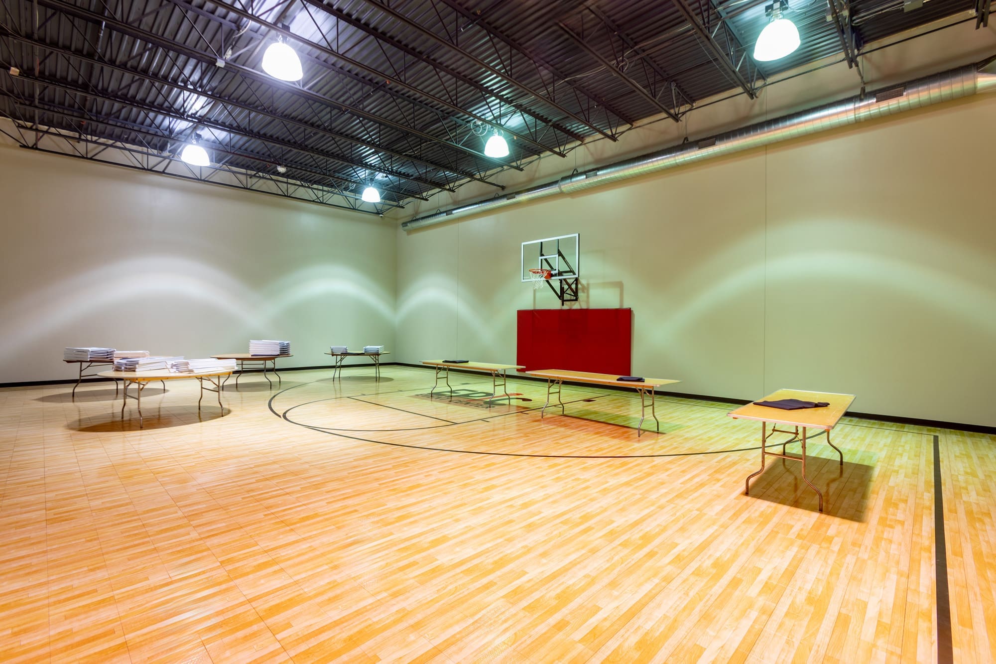 Spacious commercial indoor basketball court with hardwood floors, hoop, ample overhead lighting, and multipurpose event seating setup.