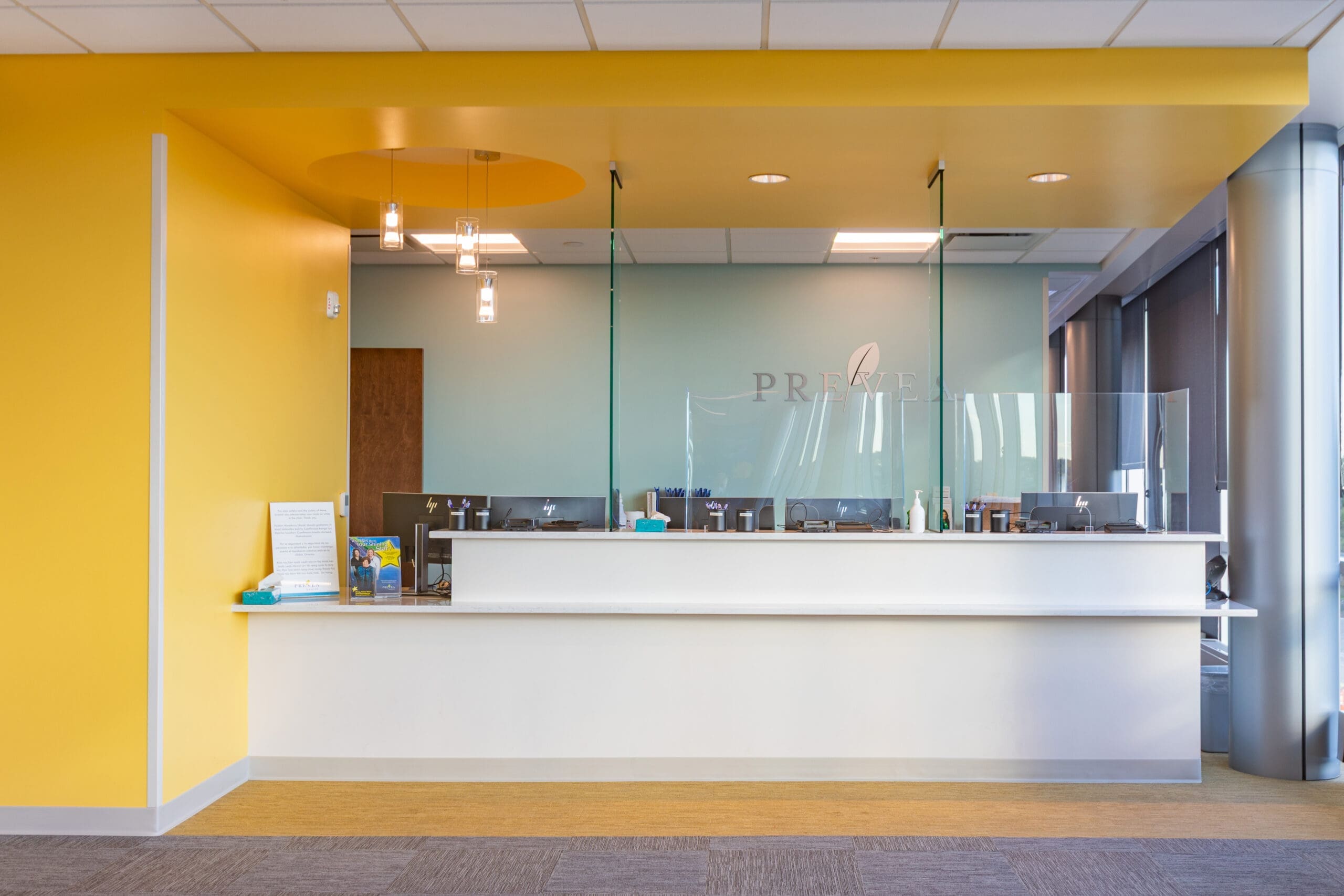 Modern commercial property reception area featuring a white front desk, glass dividers, yellow accents, and professional lighting.