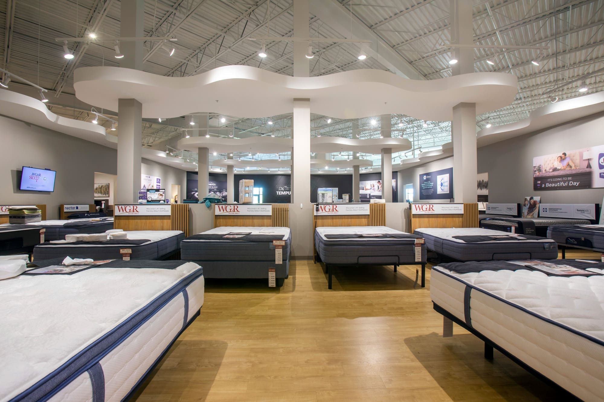 Commercial property mattress showroom featuring multiple beds, hardwood floors, high ceilings, and modern lighting—ideal retail space.