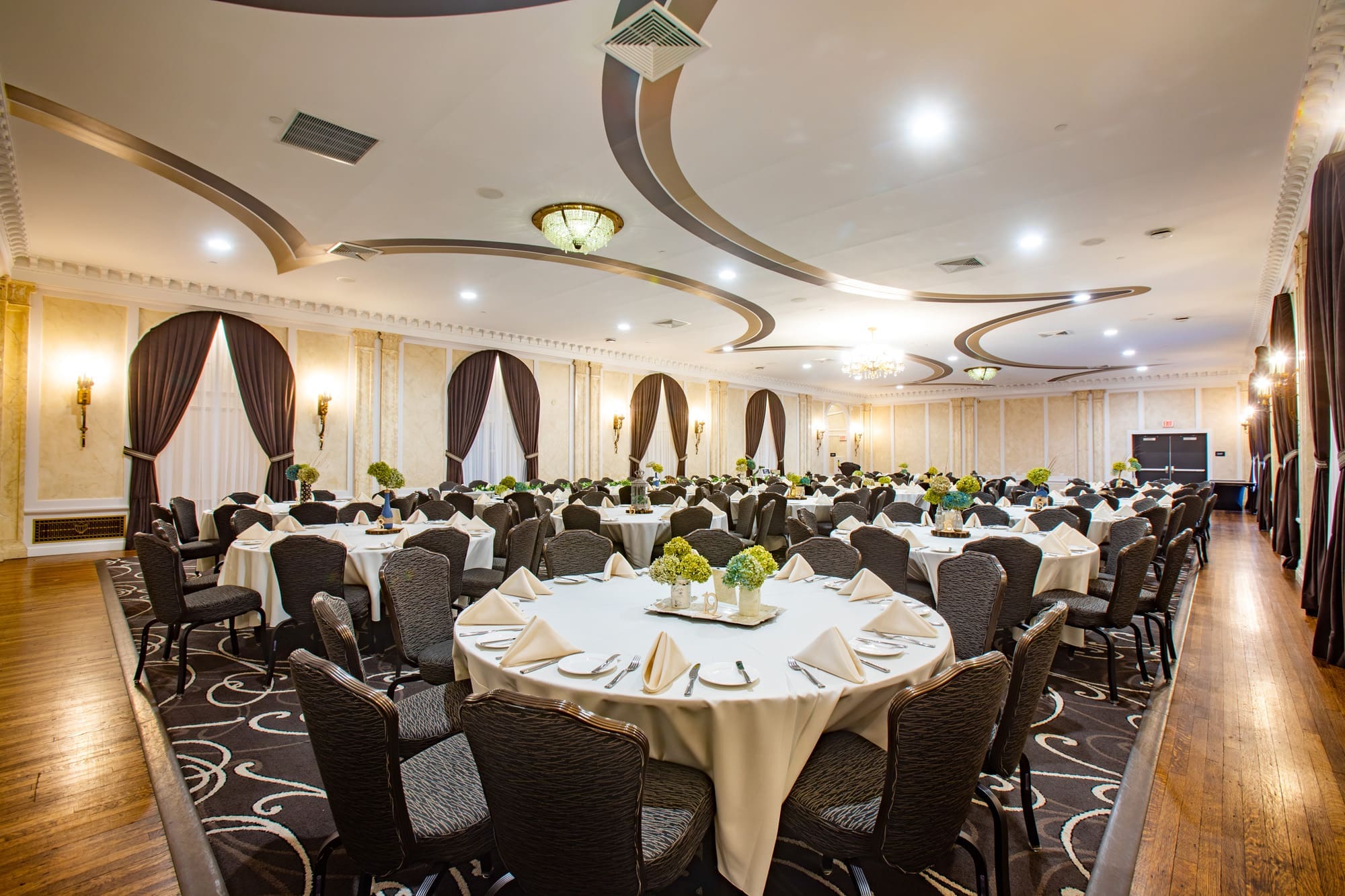 Spacious commercial banquet hall listing with round tables, elegant lighting, white linens, floral decor, and upscale event amenities.