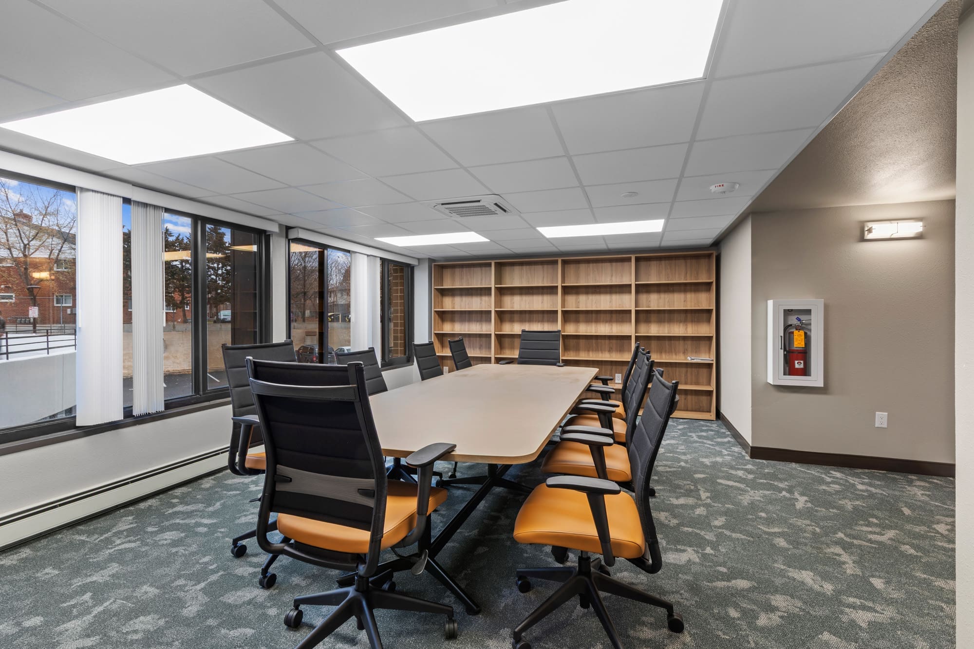 Spacious commercial conference room featuring a long table, ten chairs, built-in shelves, large windows, and bright overhead lighting.