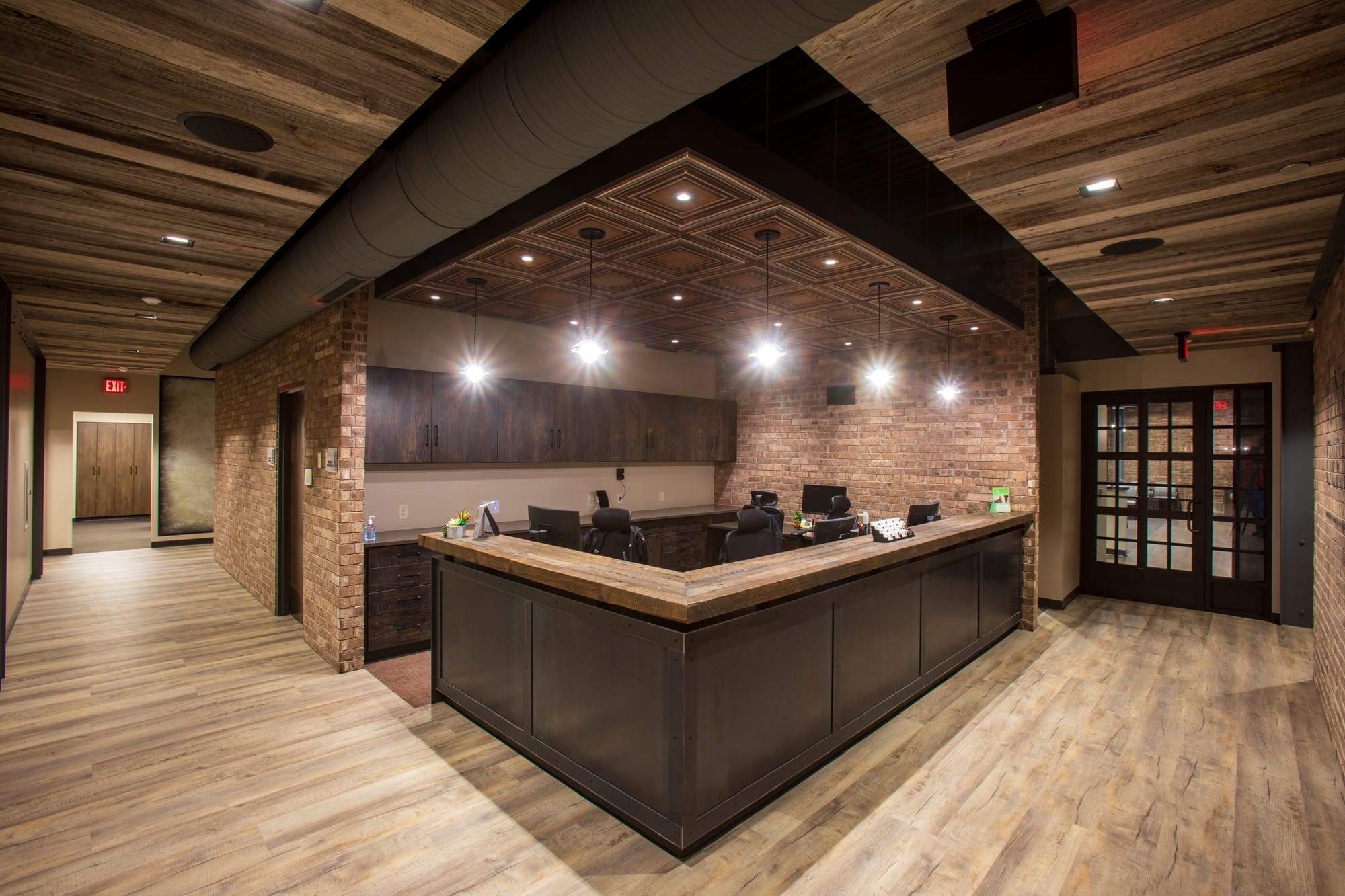 Commercial office reception with large wooden desk, exposed brick, wood floors and ceiling, seating area, and modern lighting.