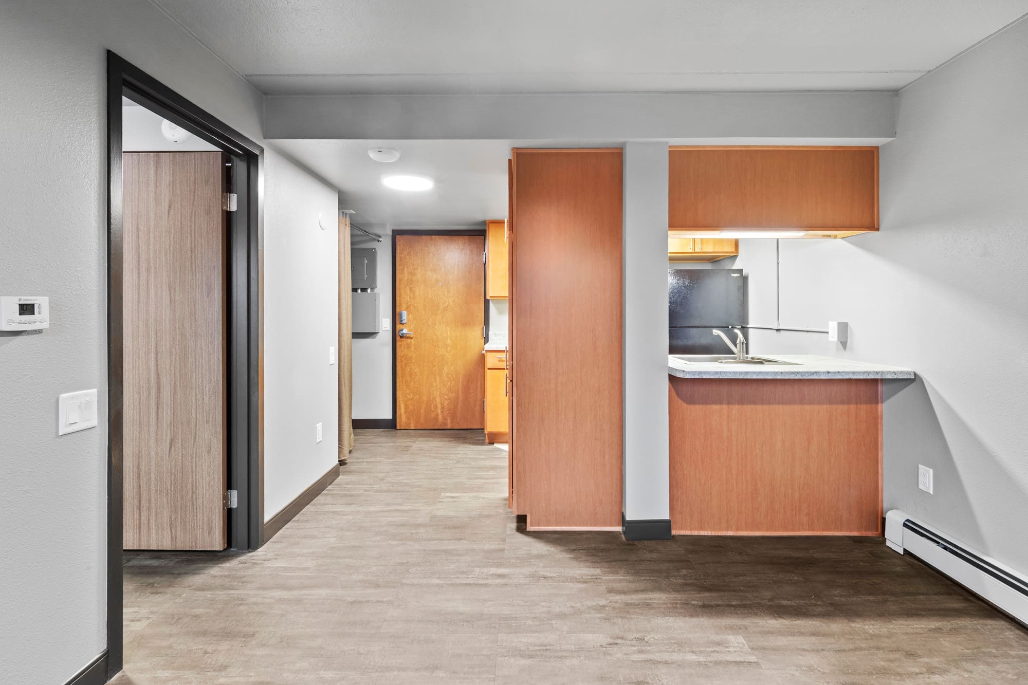 Spacious unfurnished residential apartment features wood floors, gray walls, open kitchen with wood cabinets, and access to multiple rooms.